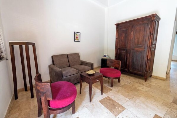 Una sala de estar con un sofá marrón, dos sillas de madera, una mesita y un mueble de madera grande.
