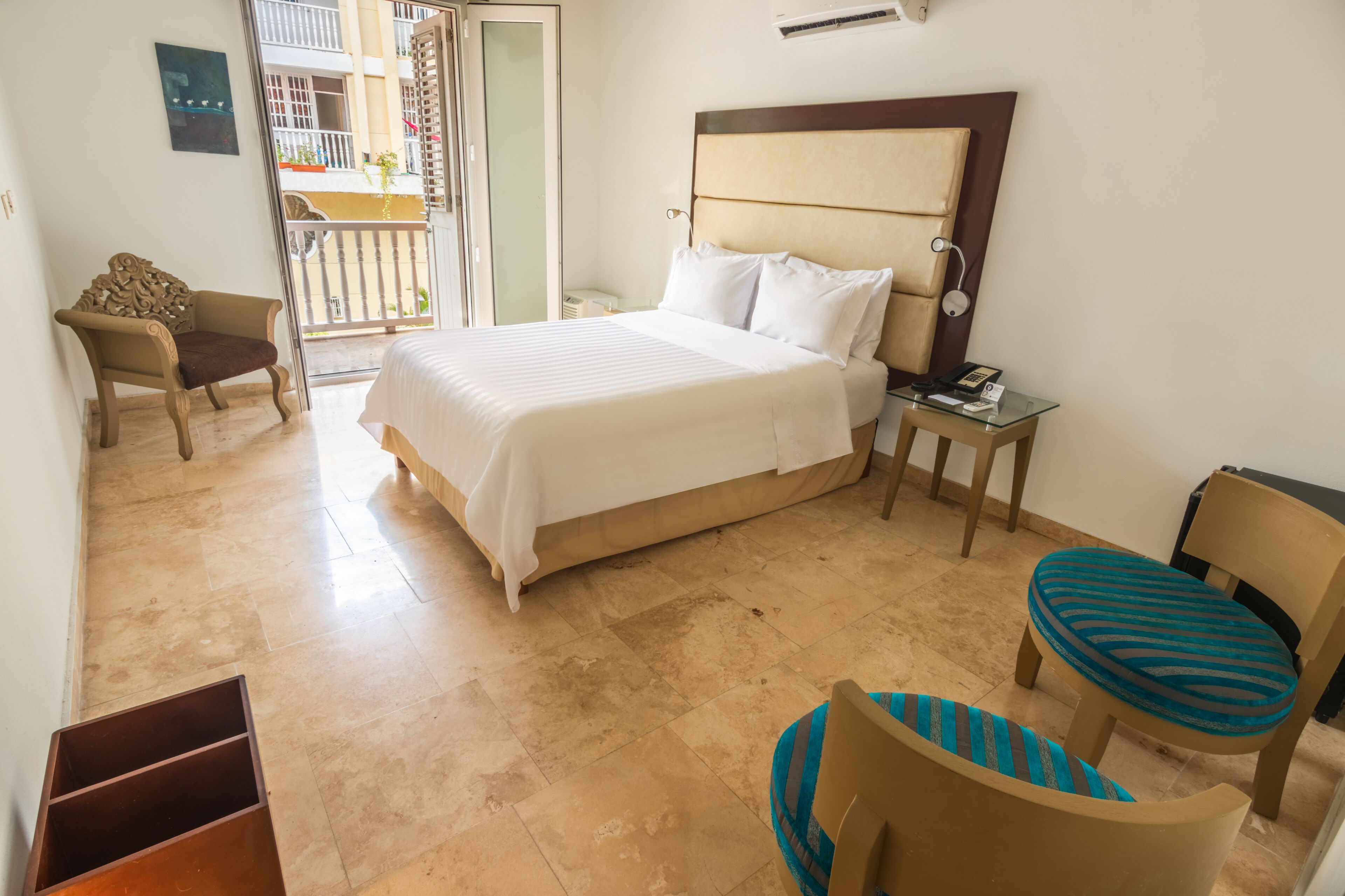 A hotel room with a bed, a chair, a small table, and a balcony.