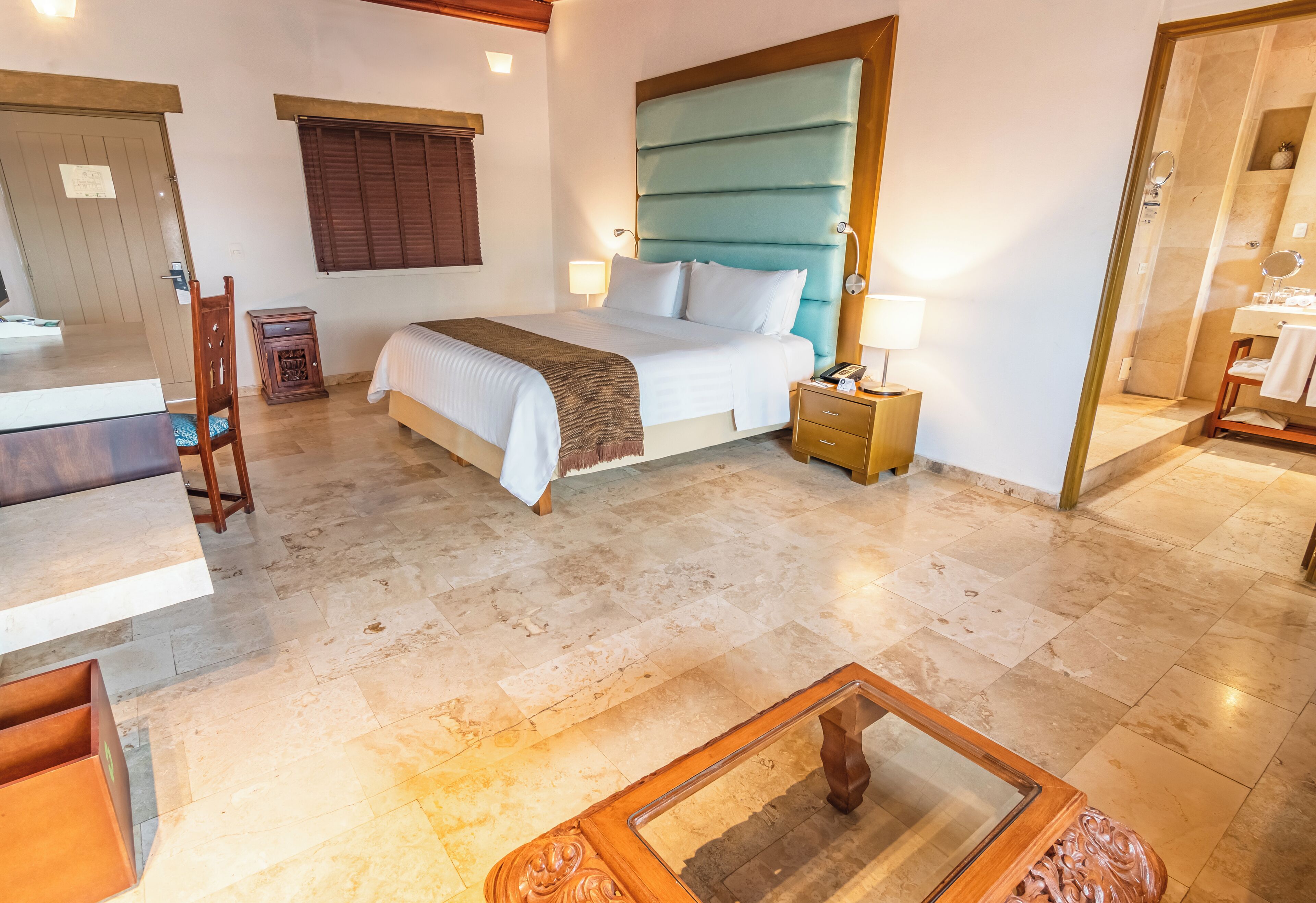 A hotel room with a bed, bedside table, lamp, and a wooden chair.