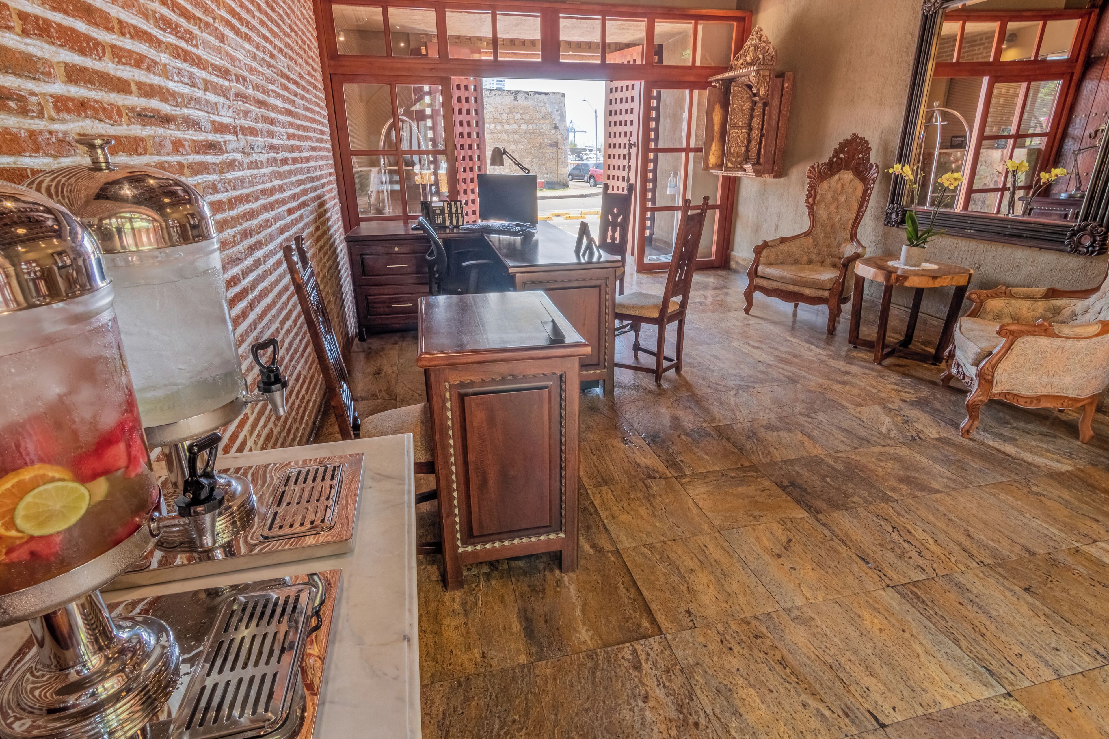 A room with a brick wall, wooden furniture, a desk with a computer, and a large window with a view of the street.