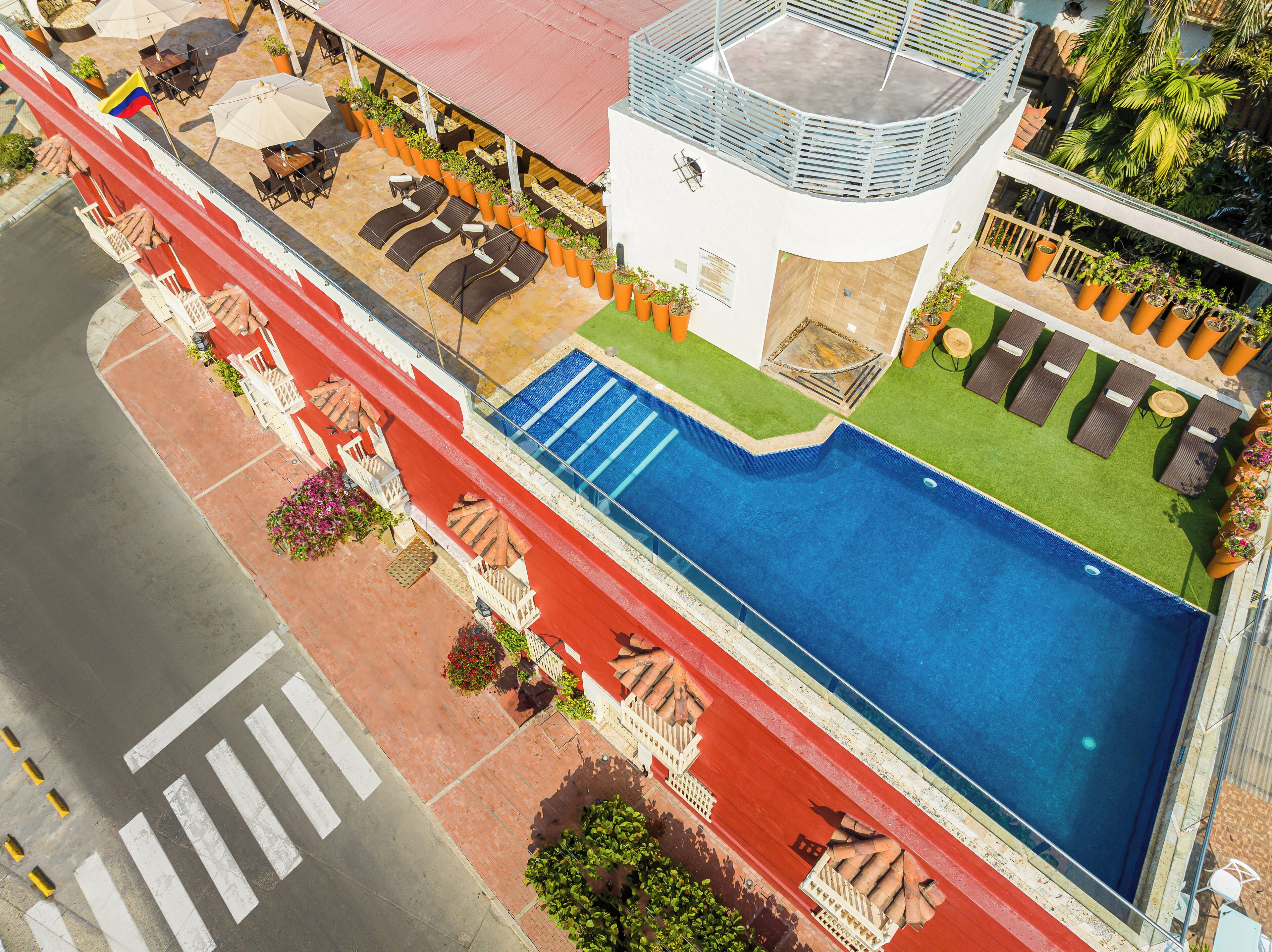 A rooftop pool with lounge chairs and umbrellas, surrounded by potted plants and a red-tiled walkway.