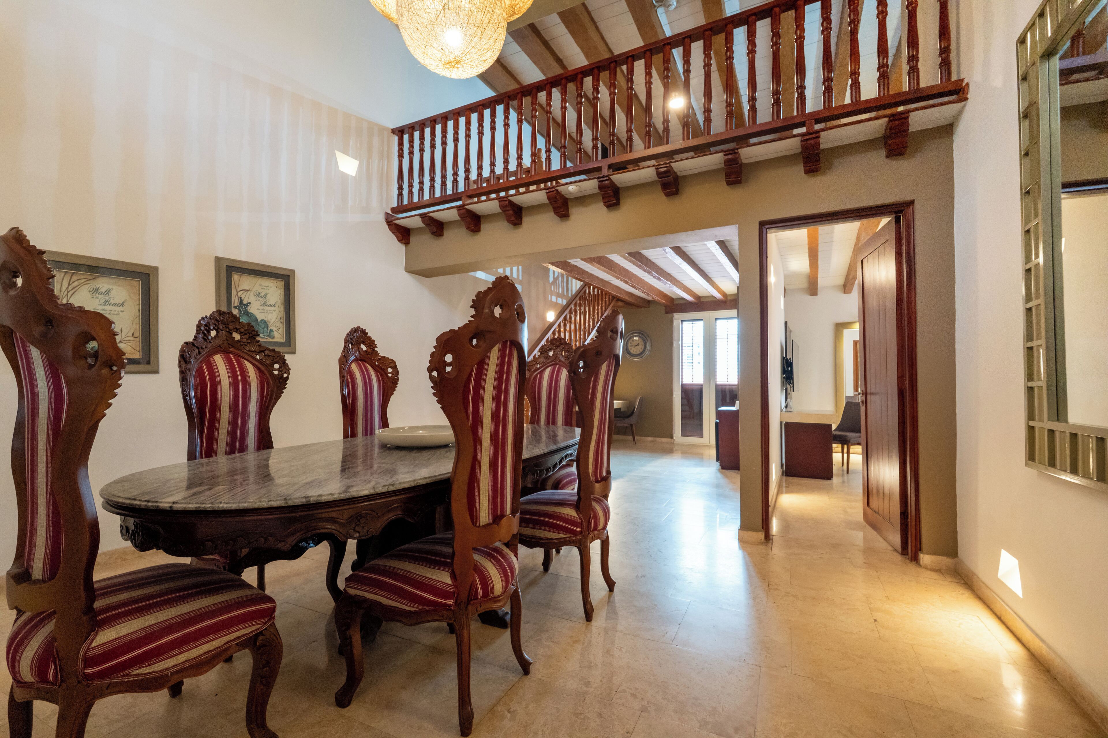 Un comedor con una mesa redonda y sillas tapizadas a rayas, una escalera de madera y vistas a otra habitación.