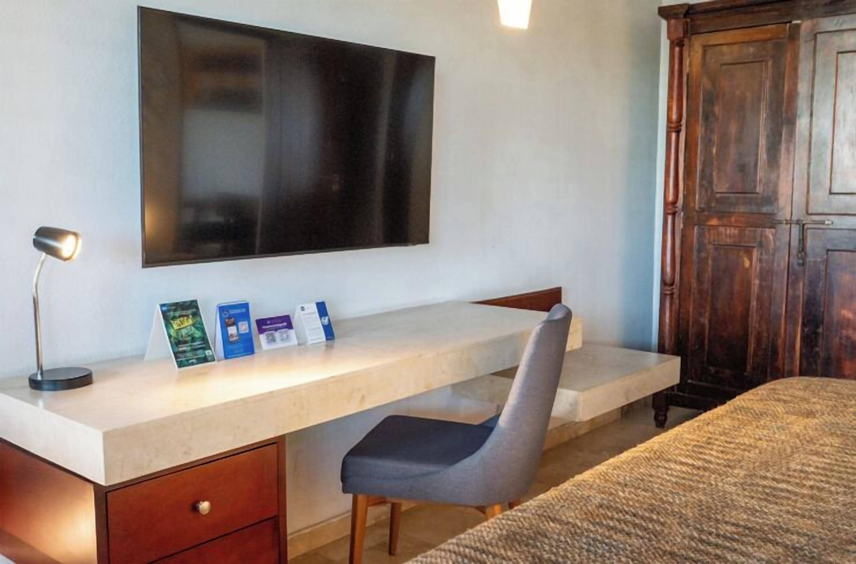A room with a desk, chair, bed, and a large wooden wardrobe.