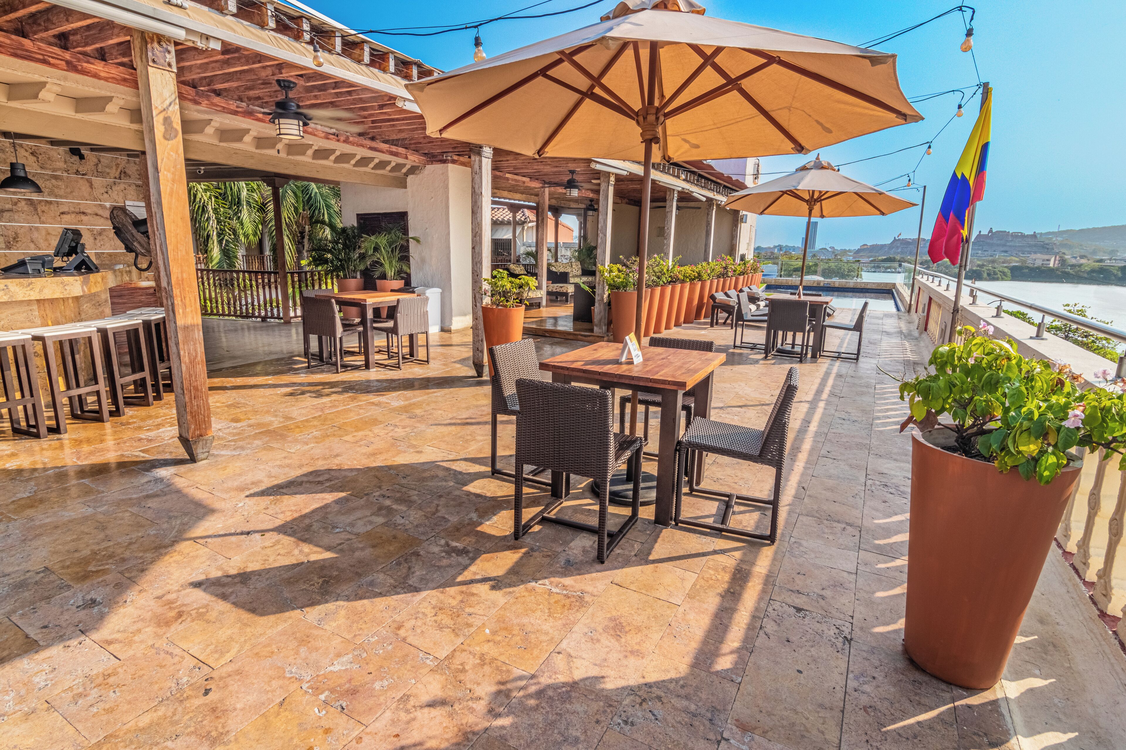 Une terrasse extérieure avec des tables et des chaises, des plantes en pot et un drapeau.