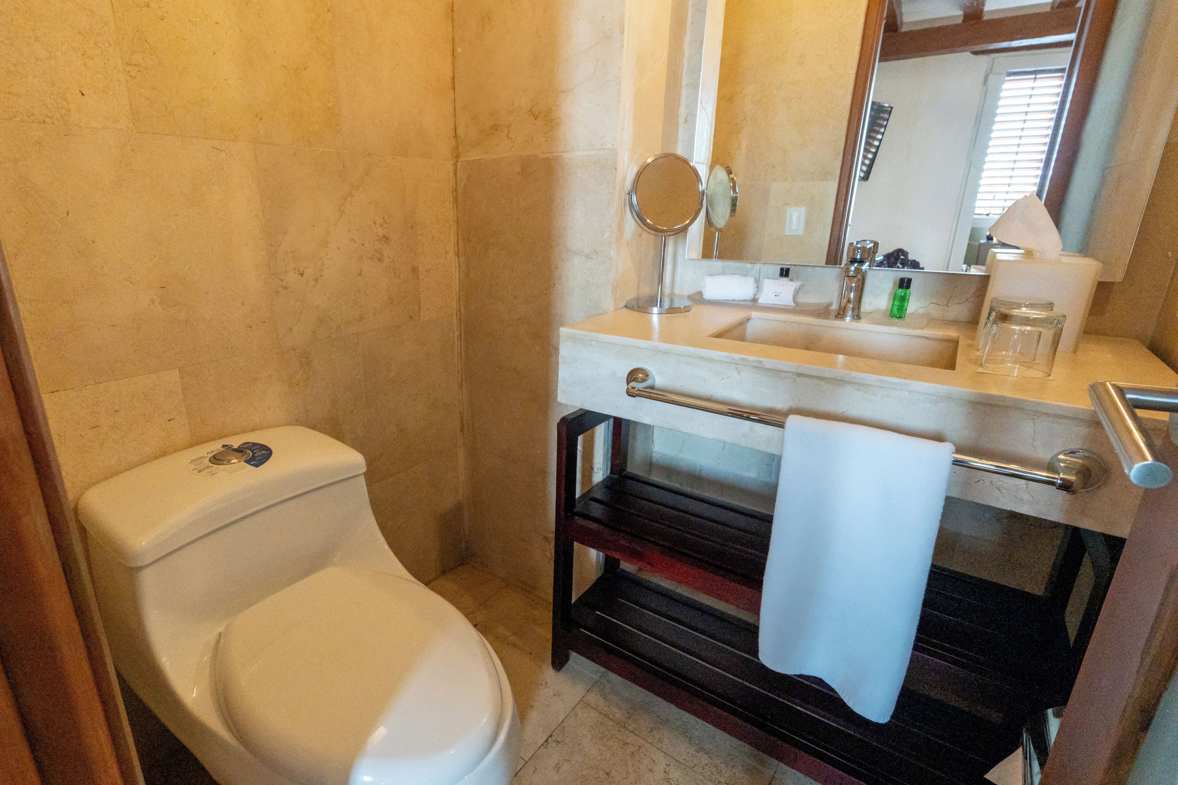 A bathroom with a toilet, sink, mirror, and towel rack.