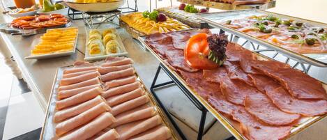 Un buffet proposant une variété de plats, notamment des viandes, des fromages et des fruits.