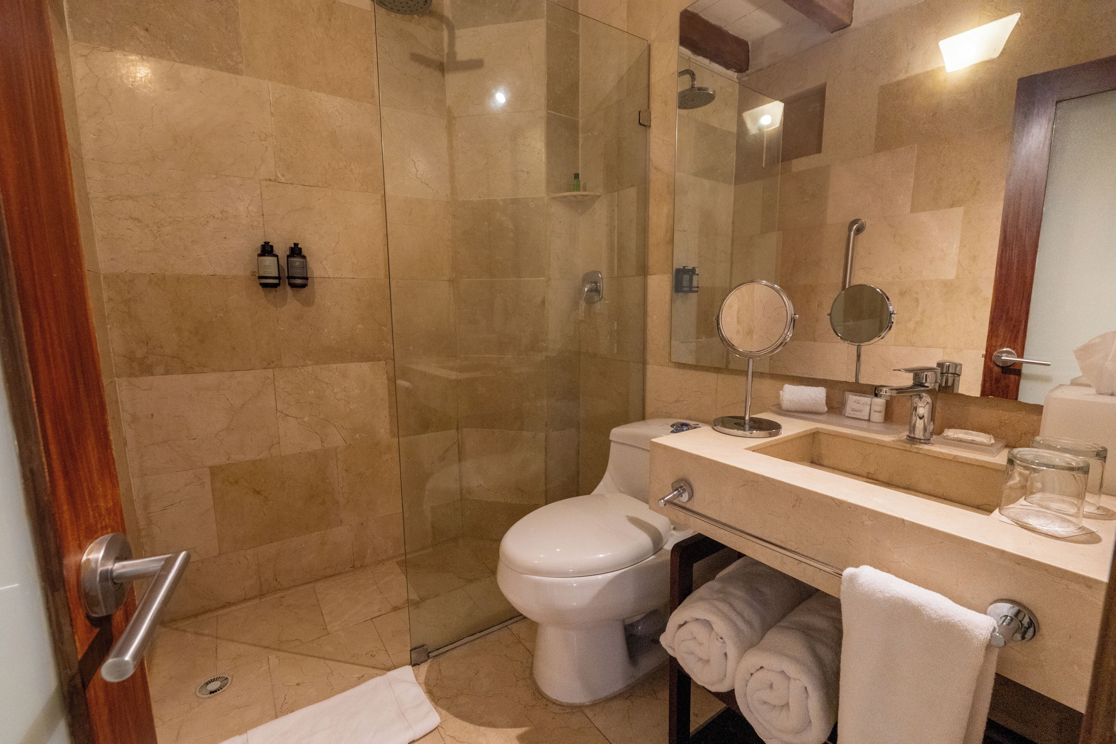 A modern bathroom with a glass-enclosed shower, a white toilet, a sink with a mirror, and two bottles of shampoo.