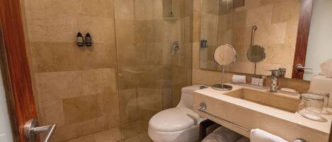 A modern bathroom with a glass-enclosed shower, a white toilet, a sink with a mirror, and two bottles of shampoo.
