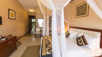 A hotel room with a bed, a desk, and a chair. There is a door leading to another room.