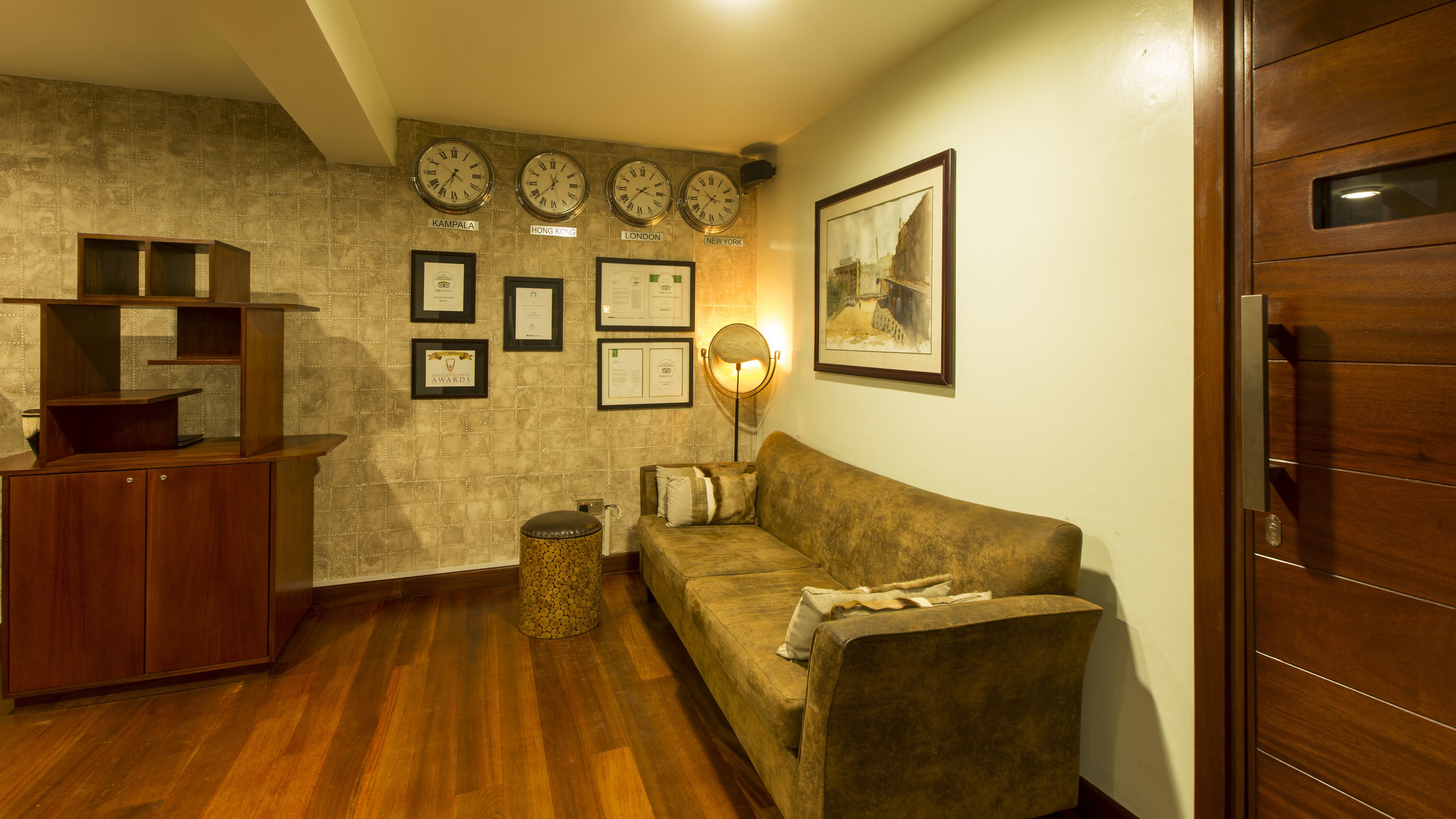 A room with a wooden floor, a brown sofa, a wooden cabinet, and clocks displaying times from different cities.