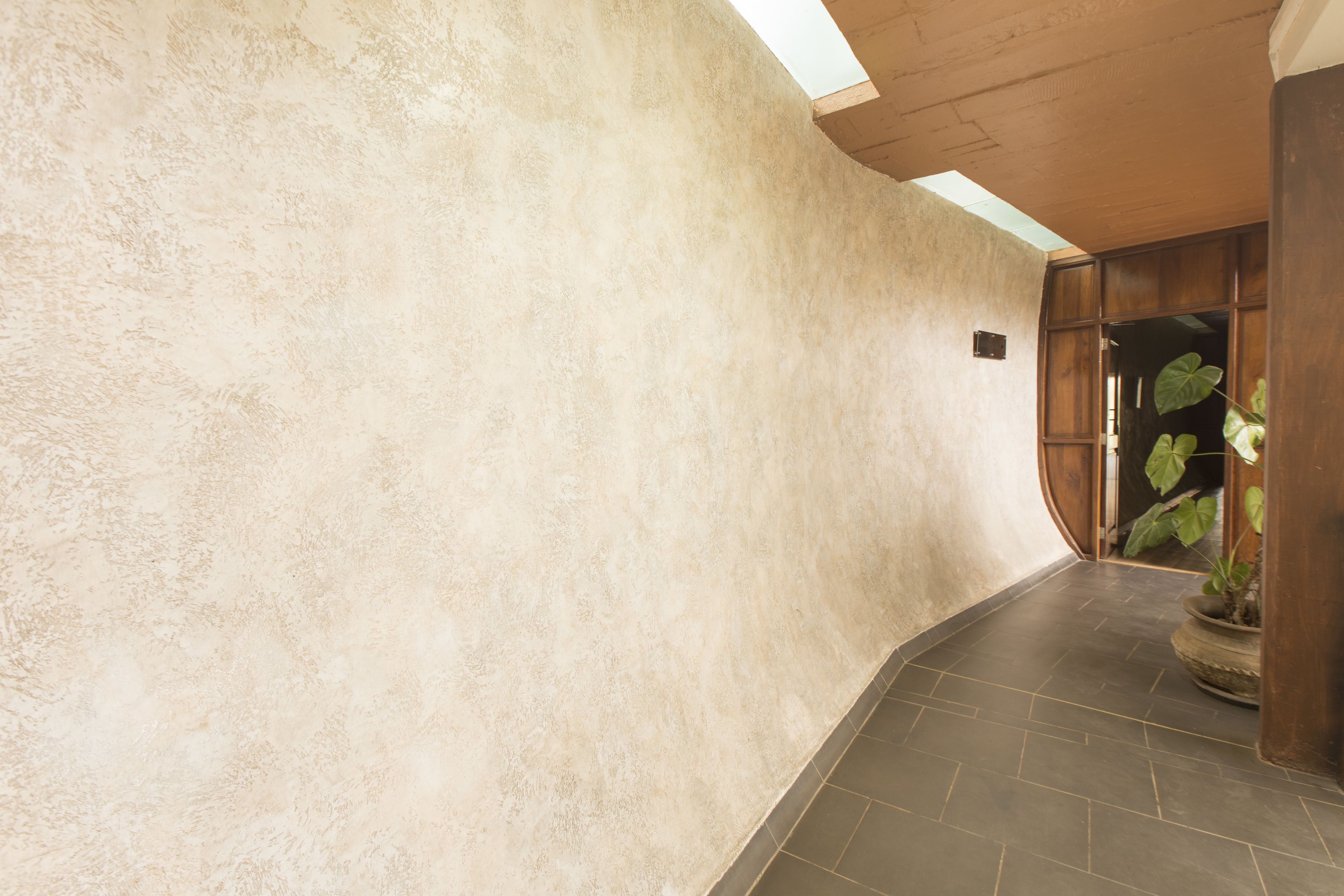 A hallway with a textured beige wall, a dark tiled floor, and a wooden door frame.