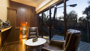 Un intérieur moderne avec un meuble en bois, une grande lampe décorative, des fauteuils en cuir, une table en marbre et de grandes fenêtres donnant sur des palmiers et une rue.