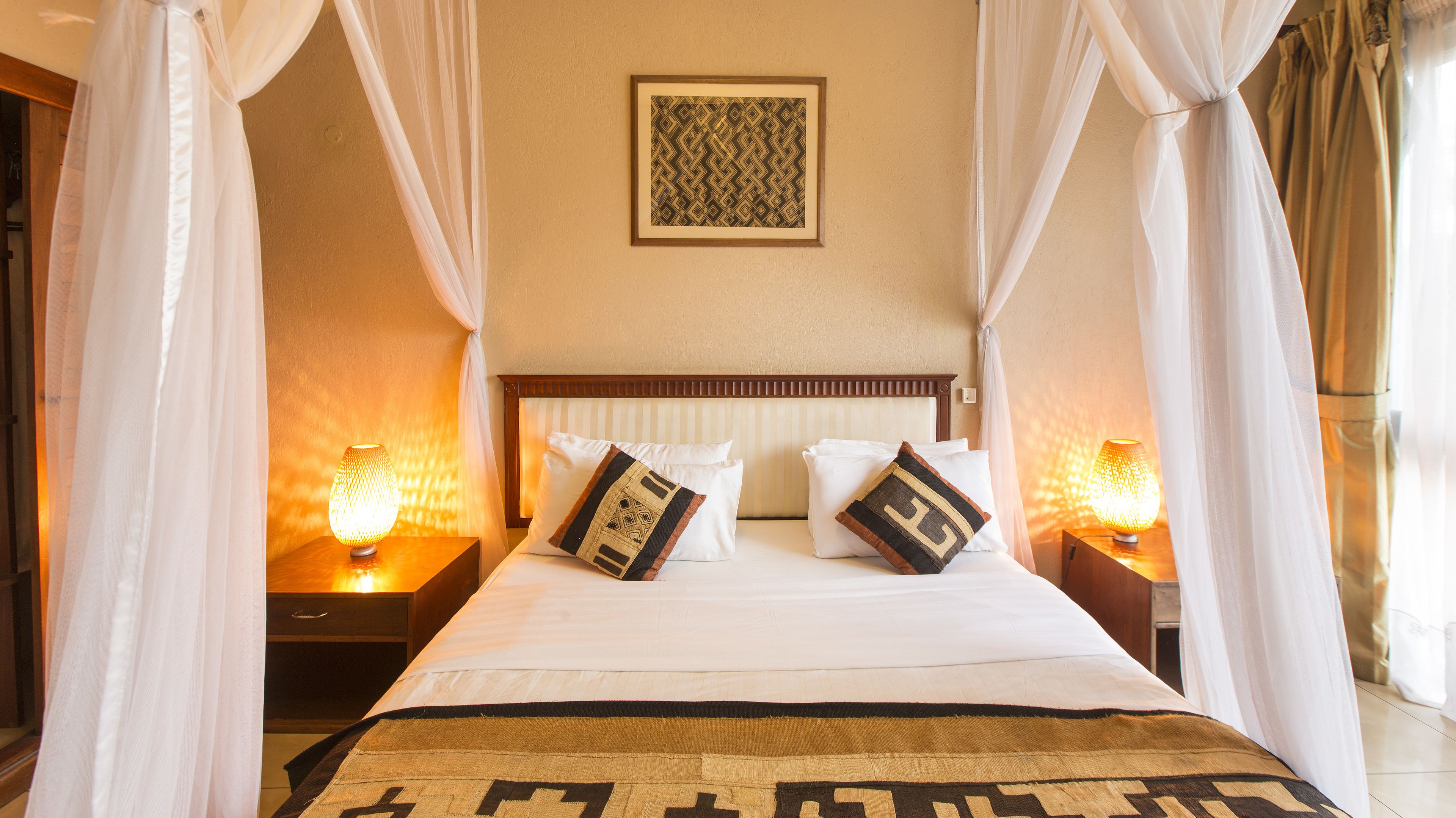 A bed with white linens, two decorative pillows, a headboard, and a bedside lamp.