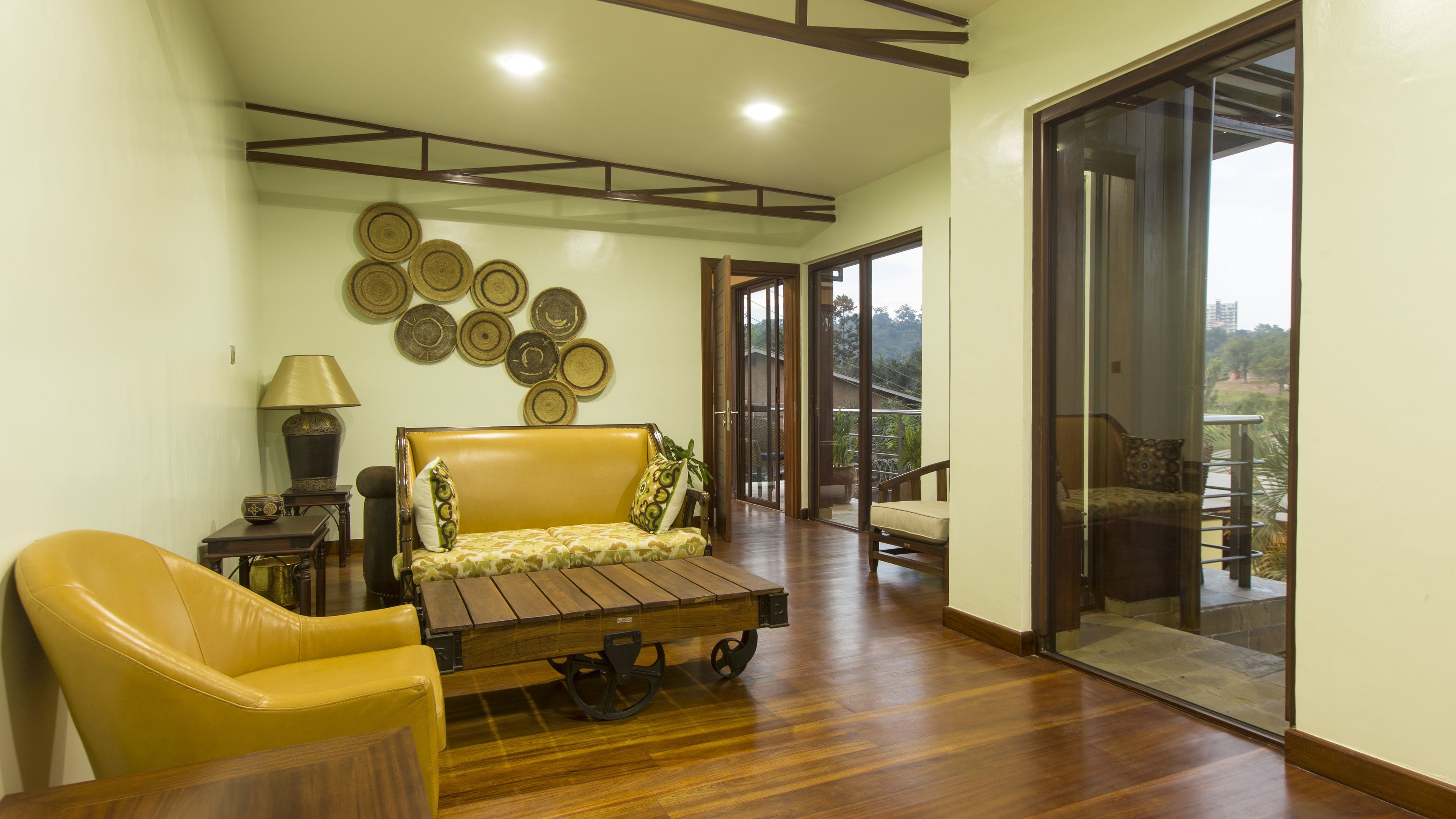 A spacious room with a wooden floor, a sofa, a chair, and a table. There are wall decorations and a view through a glass door.