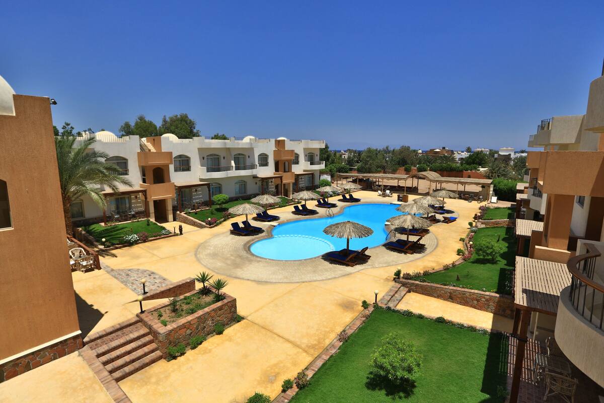 A resort with a central swimming pool, sun loungers, and umbrellas.