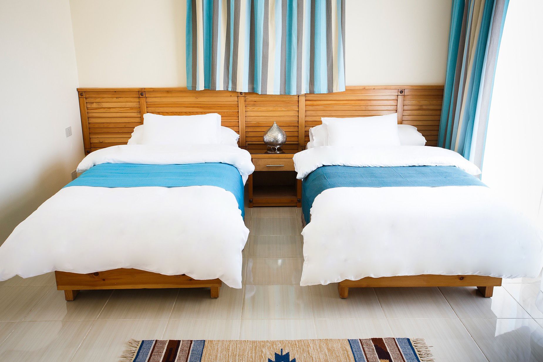 A double room with two beds, a wooden headboard, a nightstand, and a striped curtain.