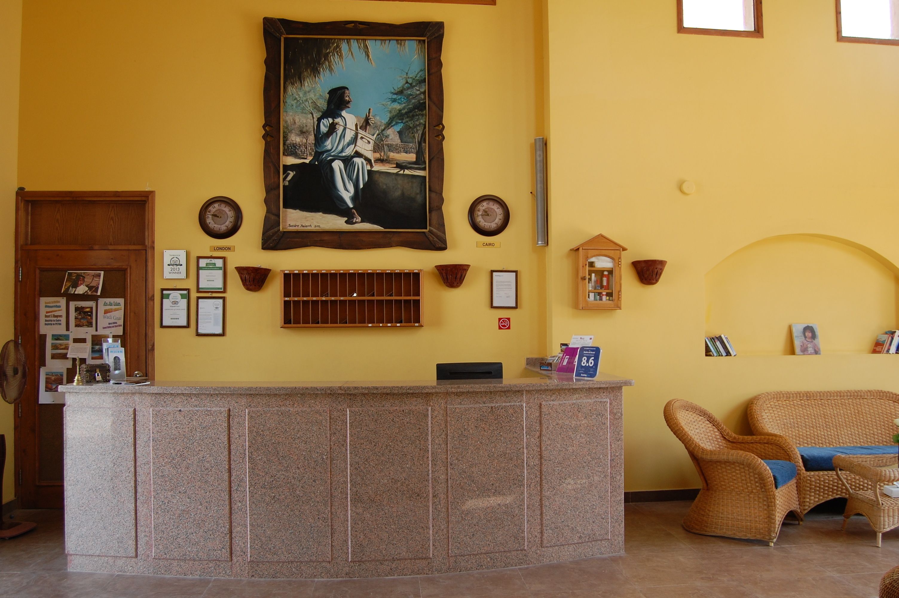 Un espace d’accueil avec un comptoir en pierre, des œuvres d’art encadrées, une horloge et un fauteuil en osier.