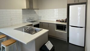 A modern kitchen with white cabinetry, a stainless steel sink, a built-in oven, a microwave, and a white refrigerator. - Southern Comfort Motel (Christchurch)