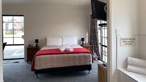 A hotel room with a bed, a nightstand, a TV, and a sign indicating spa operating hours. - Southern Comfort Motel (Christchurch)