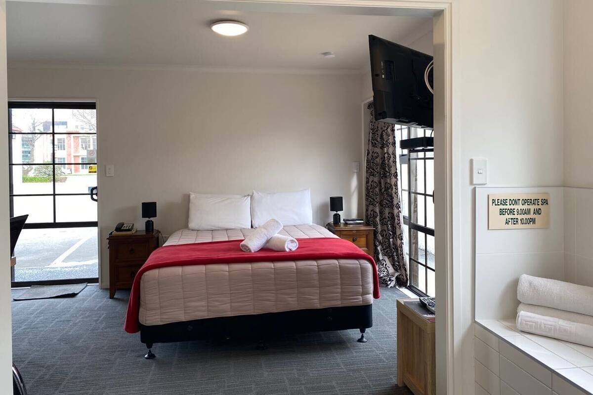 A hotel room with a bed, a nightstand, a TV, and a sign indicating spa operating hours.