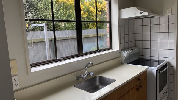 A kitchen with a window, a sink, a stove, and a tiled backsplash. - Southern Comfort Motel (Christchurch)