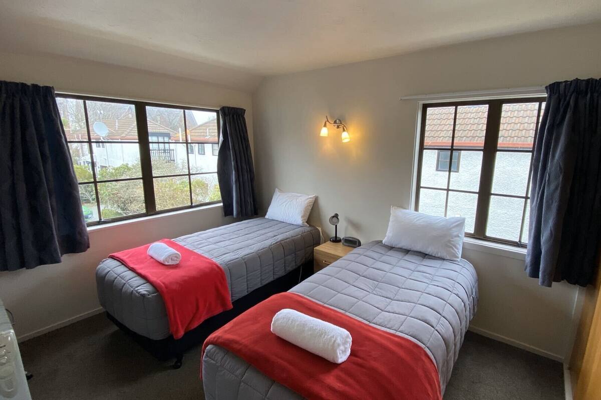 A room with two single beds, a bedside table with a lamp, and a window with curtains.