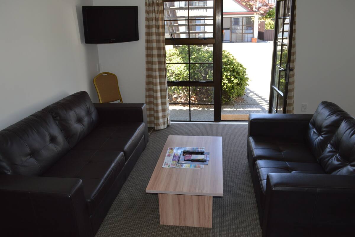 A living room with two black leather sofas, a wooden coffee table, and a television mounted on the wall.
