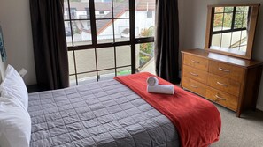 A hotel room with a bed, a wooden dresser, and a window with a view of buildings outside.