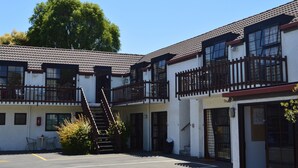 A two-story motel with a central staircase, outdoor seating, and a parking lot. - Southern Comfort Motel (Christchurch)