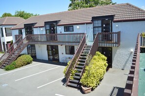 A two-story building with a tiled roof, a fenced balcony, and a parking lot. - Southern Comfort Motel (Christchurch)