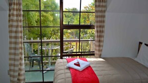 A bedroom with a large window, a bed with a red towel, and a balcony with a table and chairs. - Southern Comfort Motel (Christchurch)