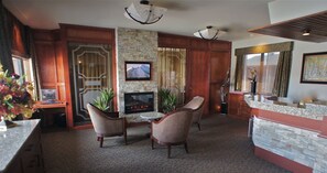 A hotel lobby with a stone fireplace, two wicker chairs, a small round table, and a television mounted on the wall. - Motel du Chevalier (Gatineau)