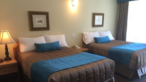 Une chambre d’hôtel avec deux lits, chacun recouvert d’une couverture bleue et agrémenté d’oreillers blancs. Il y a une lampe sur le côté gauche, une table de chevet avec un téléphone et des tableaux encadrés accrochés aux murs.