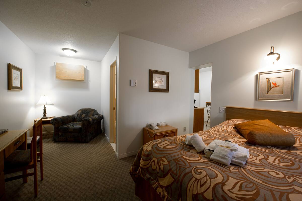 A hotel room with a bed, a desk, a chair, a lamp, and a framed picture on the wall.