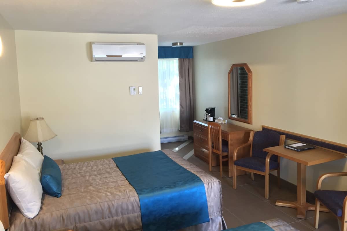 A hotel room with a bed, a desk, a chair, a lamp, an air conditioner, and a mirror.