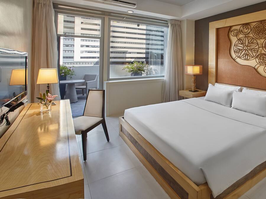 Habitación de hotel con una cama grande, dos mesitas de noche con lámparas, una silla, un escritorio con lámpara y vistas a edificios a través de la ventana.