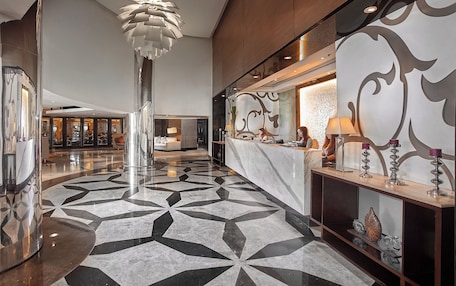 A modern lobby with a geometric patterned floor, a tall column, and a reception desk with decorative items.