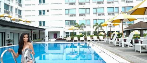 Una piscina con un edificio moderno al fondo, sillas de descanso y sombrillas.
