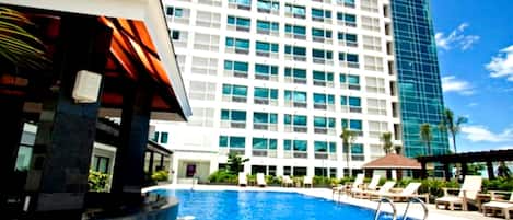 Una piscina con sillas de descanso y un edificio moderno con fachada de vidrio al fondo.