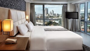 A hotel room with a large bed, a bedside lamp, a telephone, a TV, and a city view. - Quest Hotel & Conference Center (Cebu City)