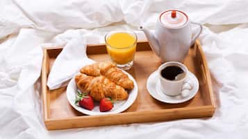 A wooden tray with croissants, strawberries, a glass of orange juice, a cup of coffee, and a teapot on a bed with white sheets.