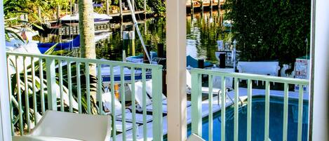 A balcony with a pool, white chairs, and a ceiling fan.