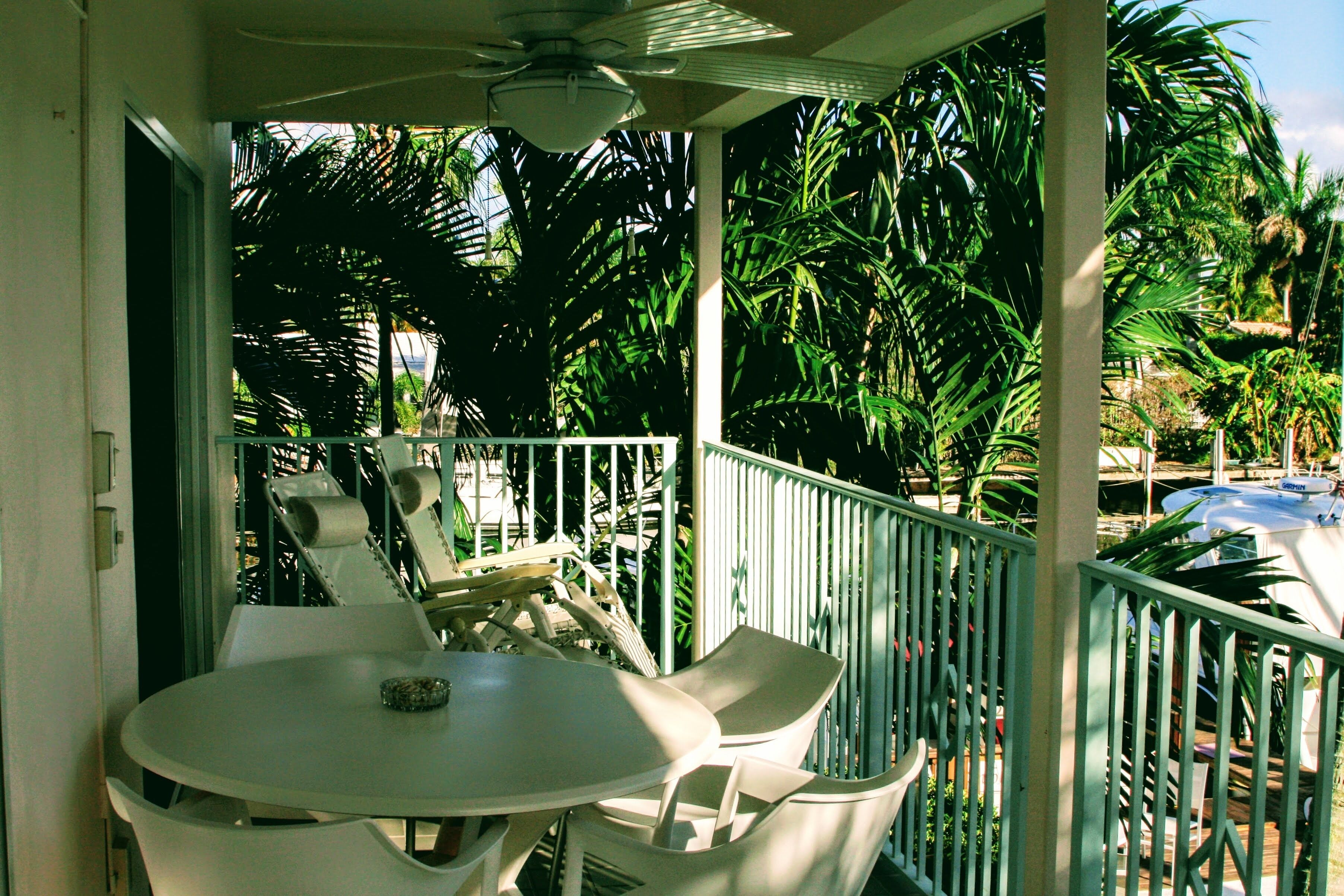 A balcony with a table and chairs, surrounded by palm trees and a pool.