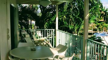 A balcony with a table and chairs, surrounded by palm trees and a pool.