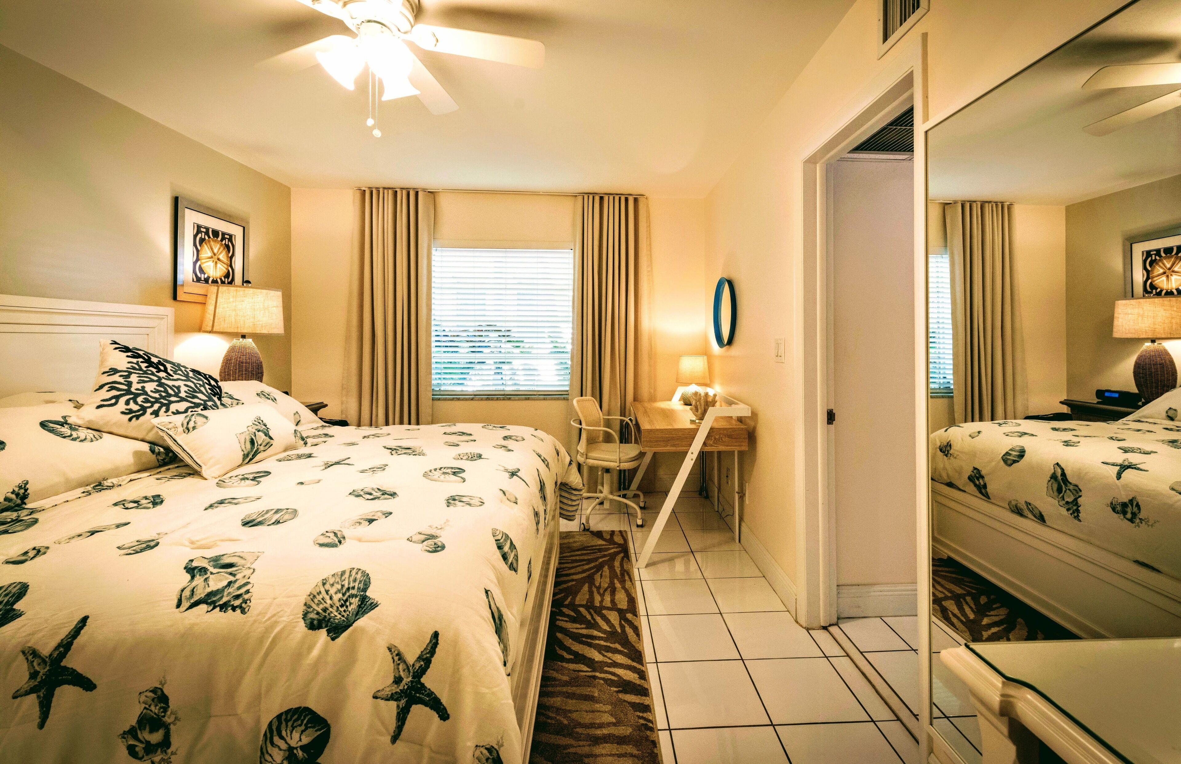 A hotel room with two beds, a desk, a chair, a ceiling fan, and a large mirror.