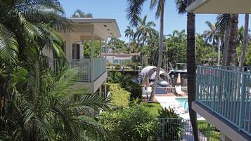 Un resort con piscina, palmeras y una zona techada con sombrillas.