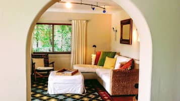 Una habitación acogedora con un sofá blanco, un pequeño reposapiés, una silla de mimbre y una alfombra estampada.