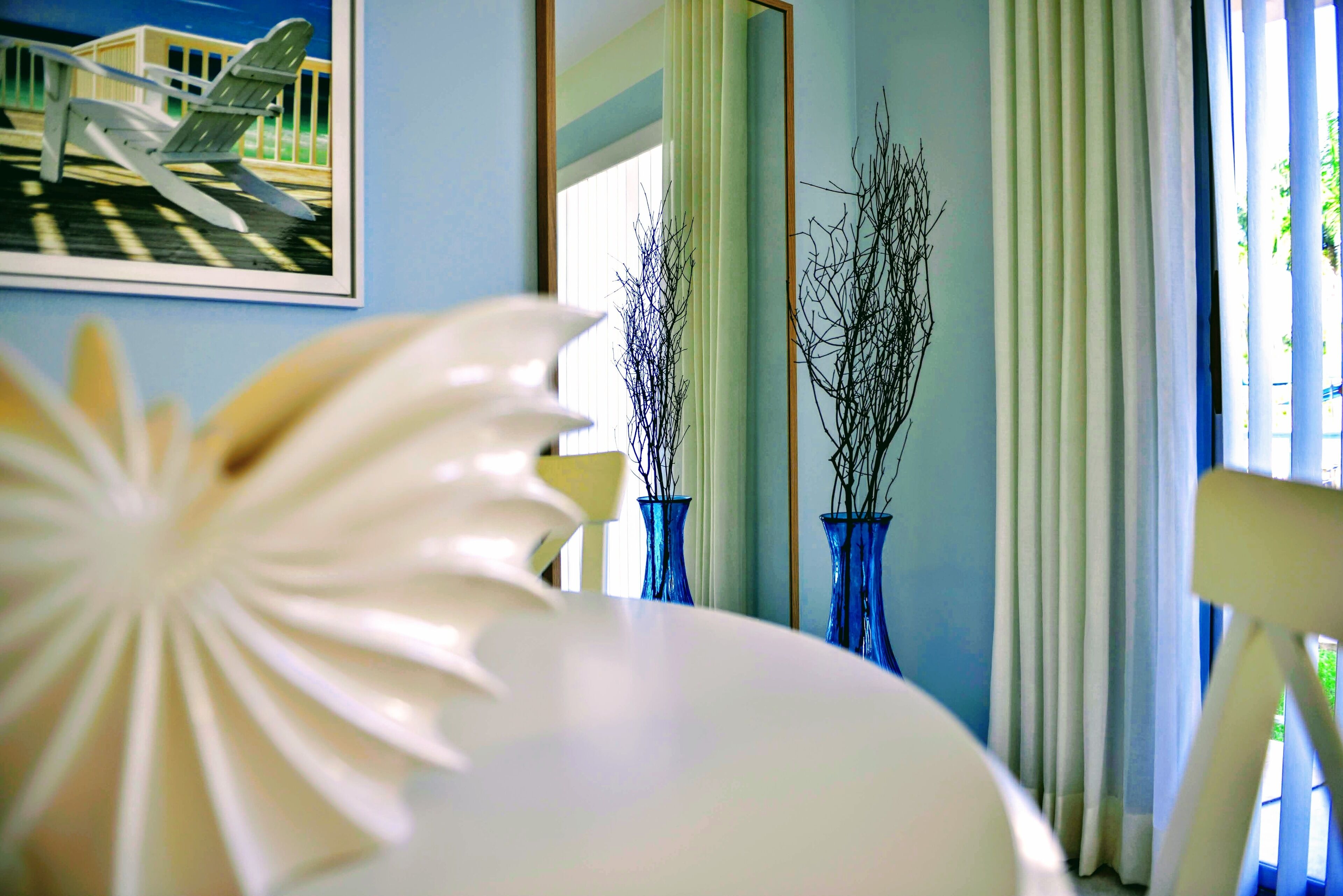 A room with a white chair, a white table, a framed picture of an airplane, and two blue vases.