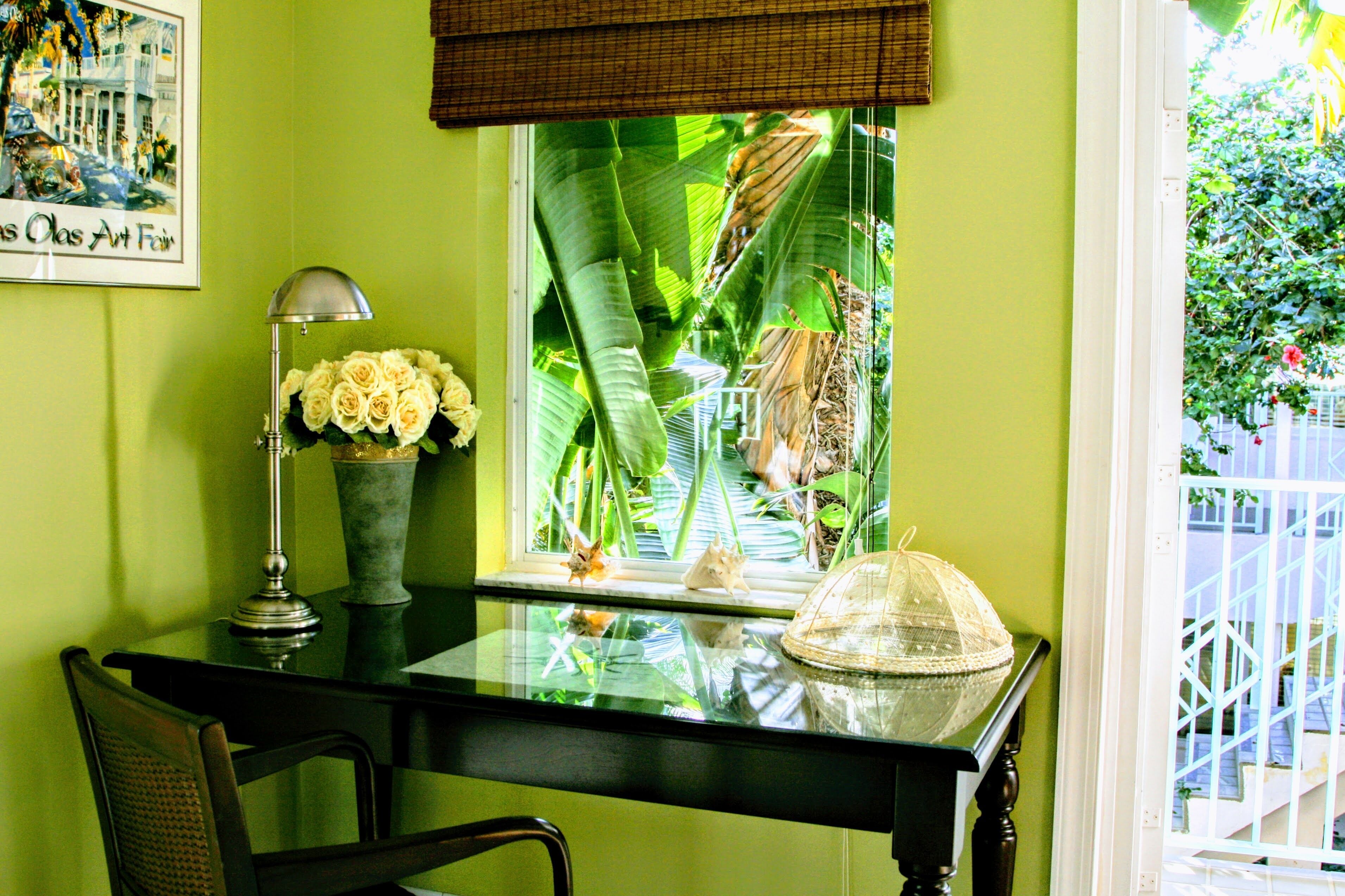 Een kamer met een glazen tafel, een stoel, een lamp, een vaas met bloemen en een raam met uitzicht op een tuin.