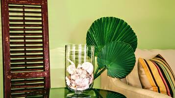 A glass bowl with seashells on a glass table, a large green leaf, and a beige sofa with striped pillows.
